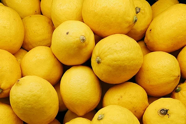 A close-up of a pile of fresh yellow lemons, showing their textured rinds and round shapes, stacked closely together.